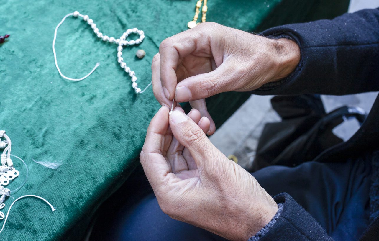Up-close photo of hands connecting beads to create a rosary necklace
