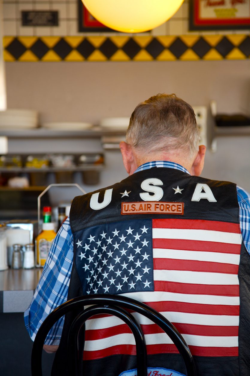 A man seated at a counter wearing an air force vest with a large american flag on the back.