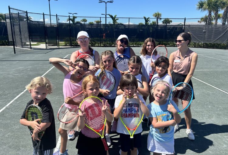 Group of kids and two adults holding tennis racquets for group photo.