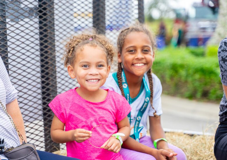 Two young girls smile at camera while taking a hay ride