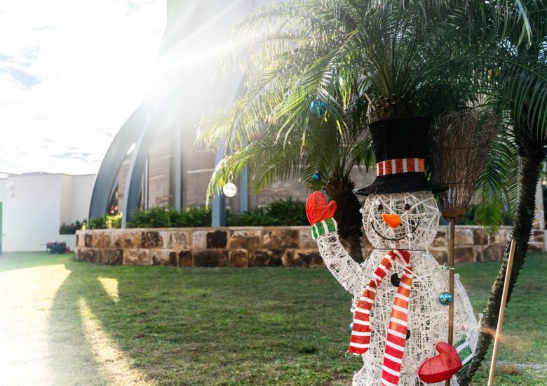 Snowman yard display in front of palm trees with the sunlight cascading in the left of the frame